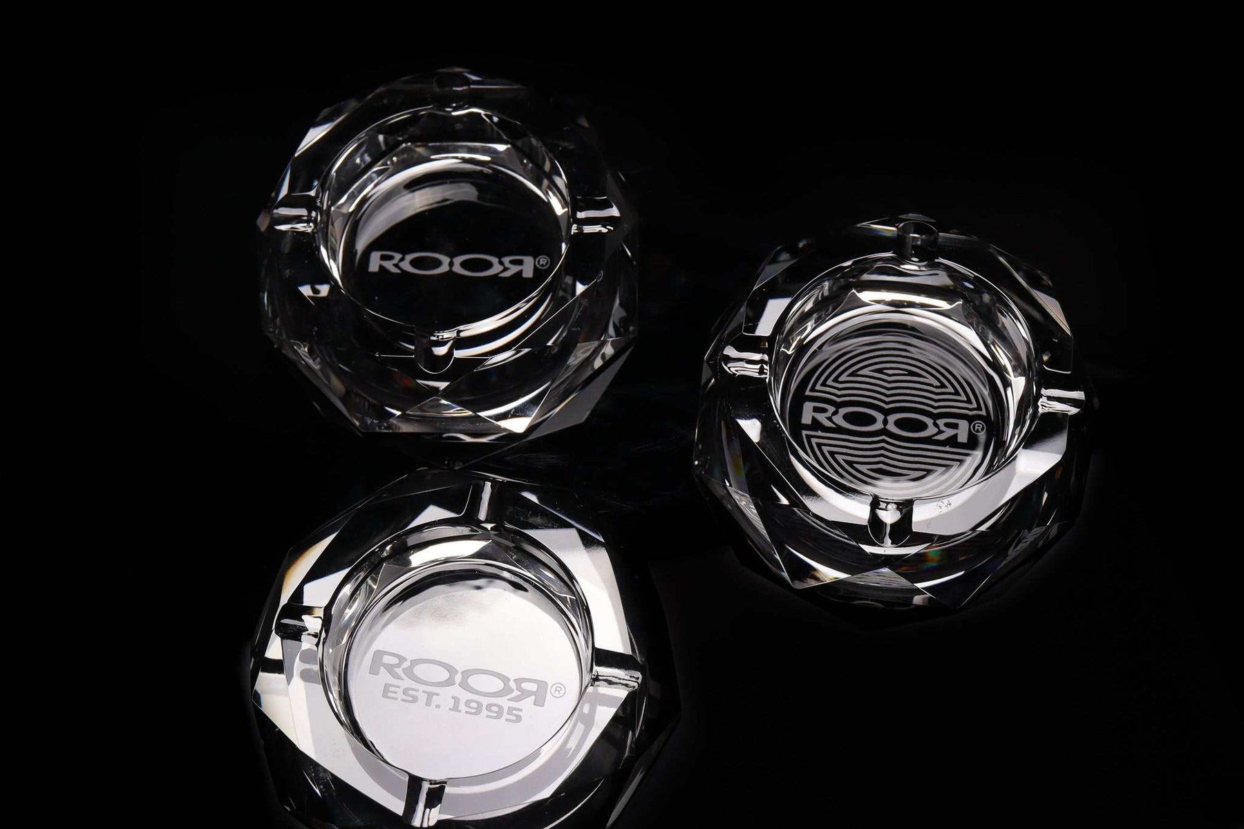 Set of three ROOR Glass Crystal Cut Ashtrays with distinctive engraved designs on a black background