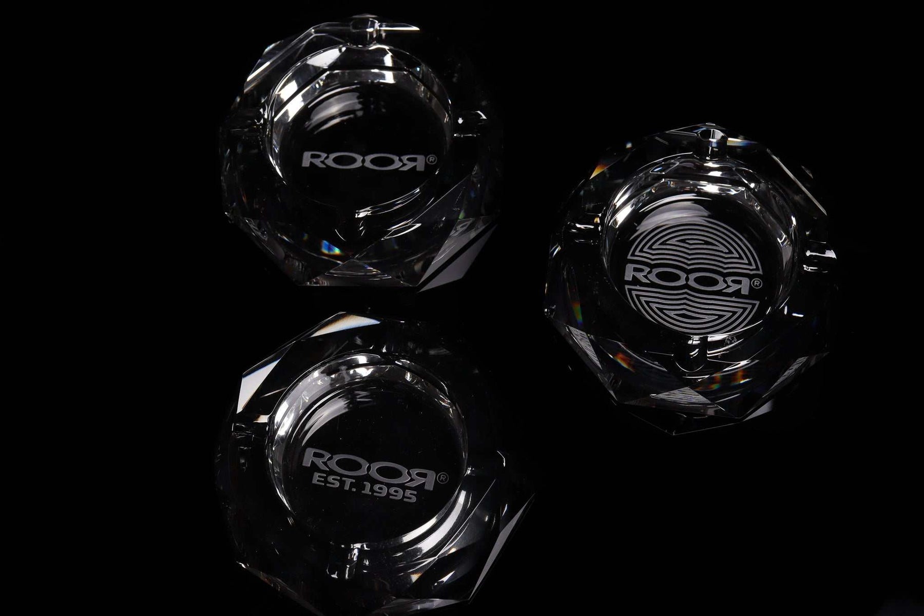 Three ROOR glass crystal cut ashtrays with engraved logos on a black background
