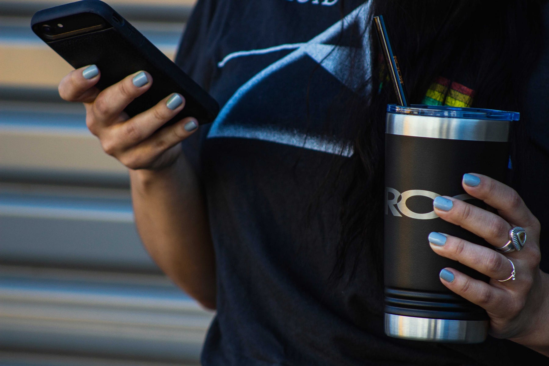 Person holding black ROOR Tumbler 16oz stainless steel laser-engraved with slider lid and smartphone