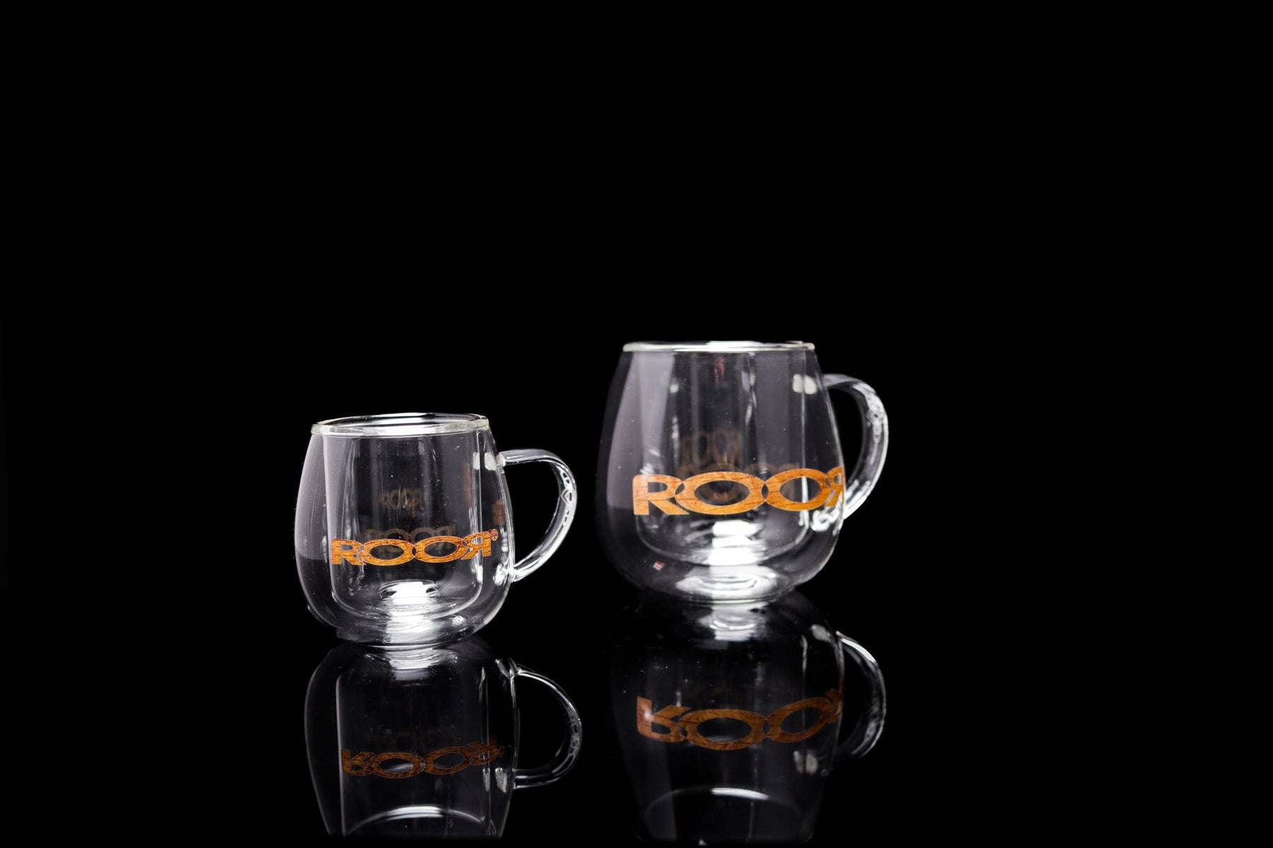 ROOR® Glass Mugs Double Layer, sleek double-walled design, transparent with orange logo, set on reflective surface.